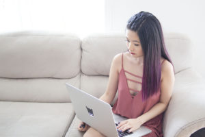 Asian woman on laptop browsing on couch.