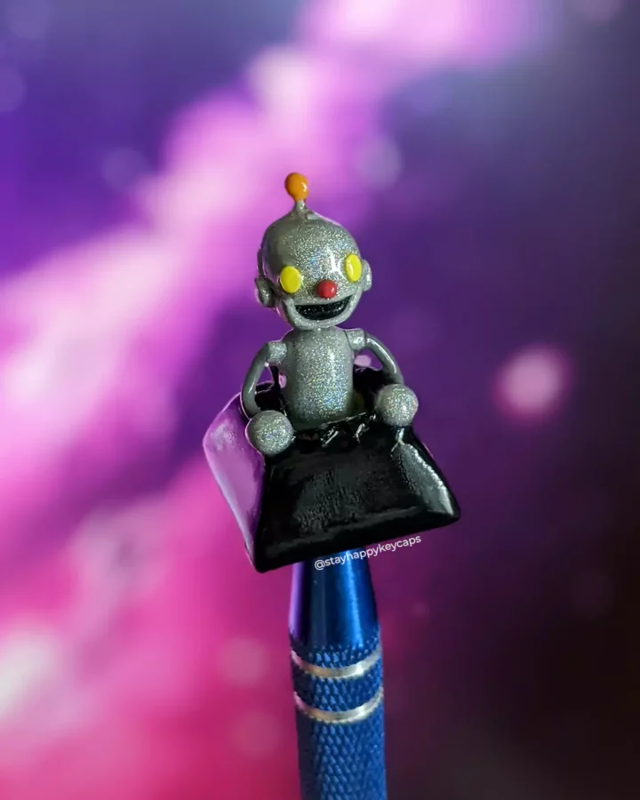 SladeByBlade Robot Artisan Keycap on a mechanical keyboard front view against a galaxy background.